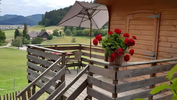 Eine Holzterrasse mit einer Treppe zu einem überdachten Bereich, einem Tisch mit Stühlen und einem großen Sonnenschirm.