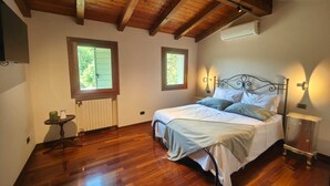 A bedroom with a wooden ceiling, a bed with white bedding, two windows, a radiator, and a small table with a lamp. - The House on the Mount - Euganean Hills Regional Park - (Veneto)