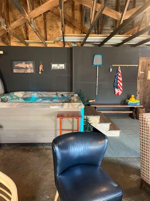 A rustic room with a wooden ceiling, a hot tub, a black leather chair, and a small table with a flag.