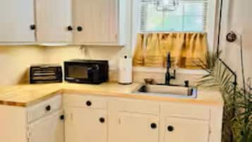 Una cocina con gabinetes blancos, un microondas y un fregadero.