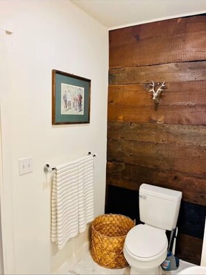 A bathroom with a wooden wall, a framed picture, a white toilet, and a woven basket.