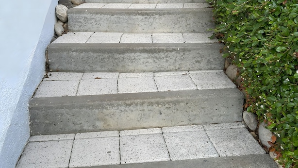 Betoninen portaikko, jossa on kiviset askelmat ja metallinen kaide, johtaa ylös valkoiselle seinälle, jonka edessä on patsas.