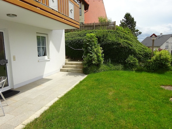 A residential property with a white exterior, a wooden balcony, a red roof, and a well-maintained lawn.