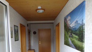 Käytävän katto on tehty puusta, siellä on ovi, pieni kaappi ja seinällä oleva kehystetty kuva.