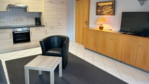 Kompakti keittiö, jossa on sisäänrakennettu uuni, musta nahkainen tuoli, pieni pöytä ja televisio, joka on sijoitettu puiseen kaappiin.