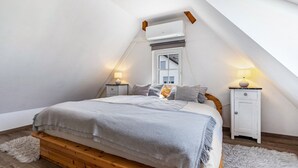 Une chambre avec un plafond en pente, un lit avec un cadre en bois, une table de chevet blanche, une lampe et un tapis moelleux.