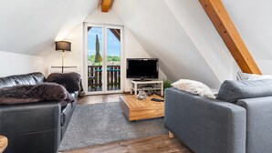 Une chambre de style loft moderne avec un plafond en pente, une grande fenêtre, un téléviseur à écran plat et un coin salon confortable avec un canapé et un fauteuil.