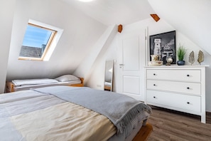 Quarto com teto inclinado, claraboia, cama, penteadeira e quadro na parede.
