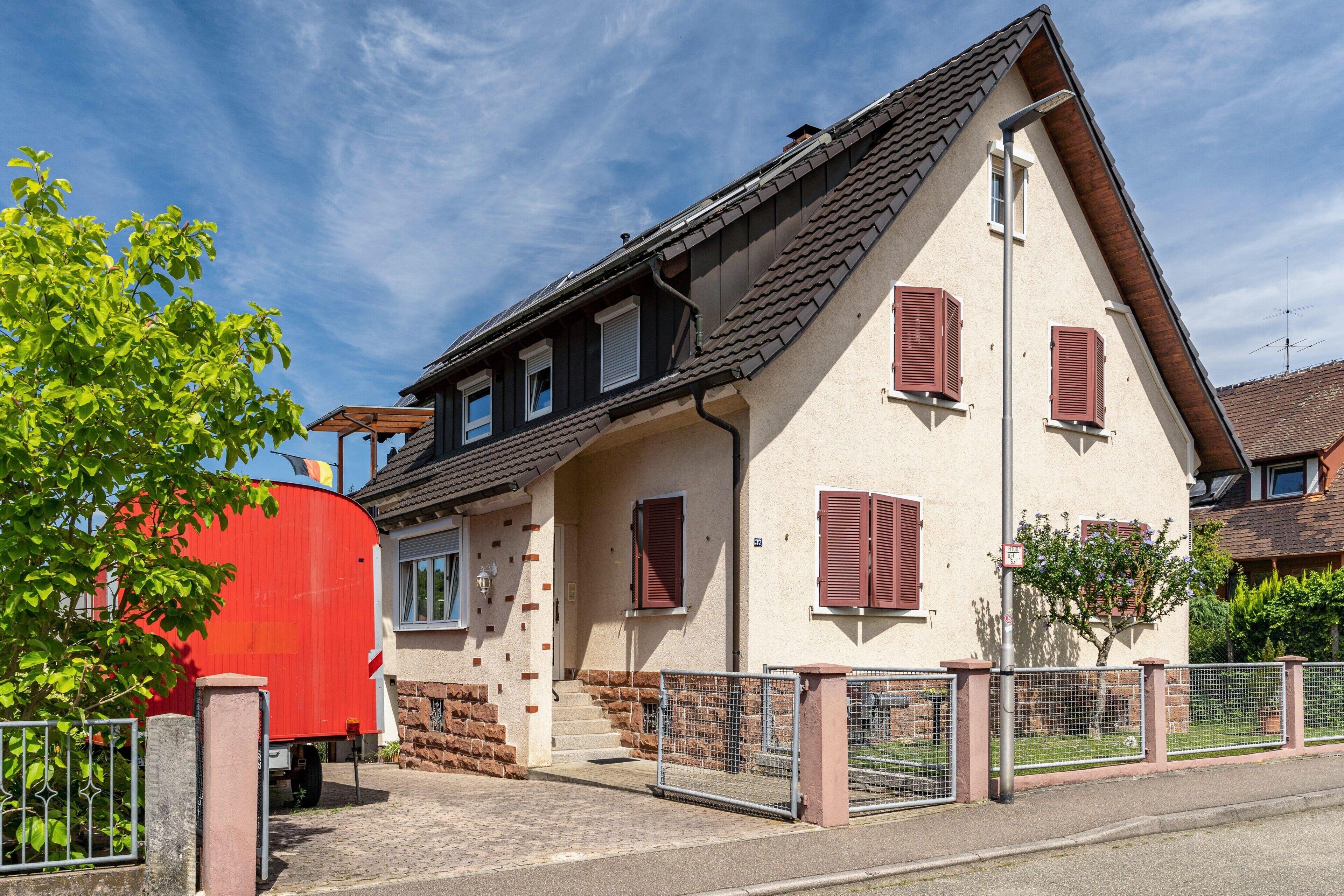 Ein zweistöckiges Haus mit einem roten Tank davor, einer befestigten Auffahrt und blauem Himmel.