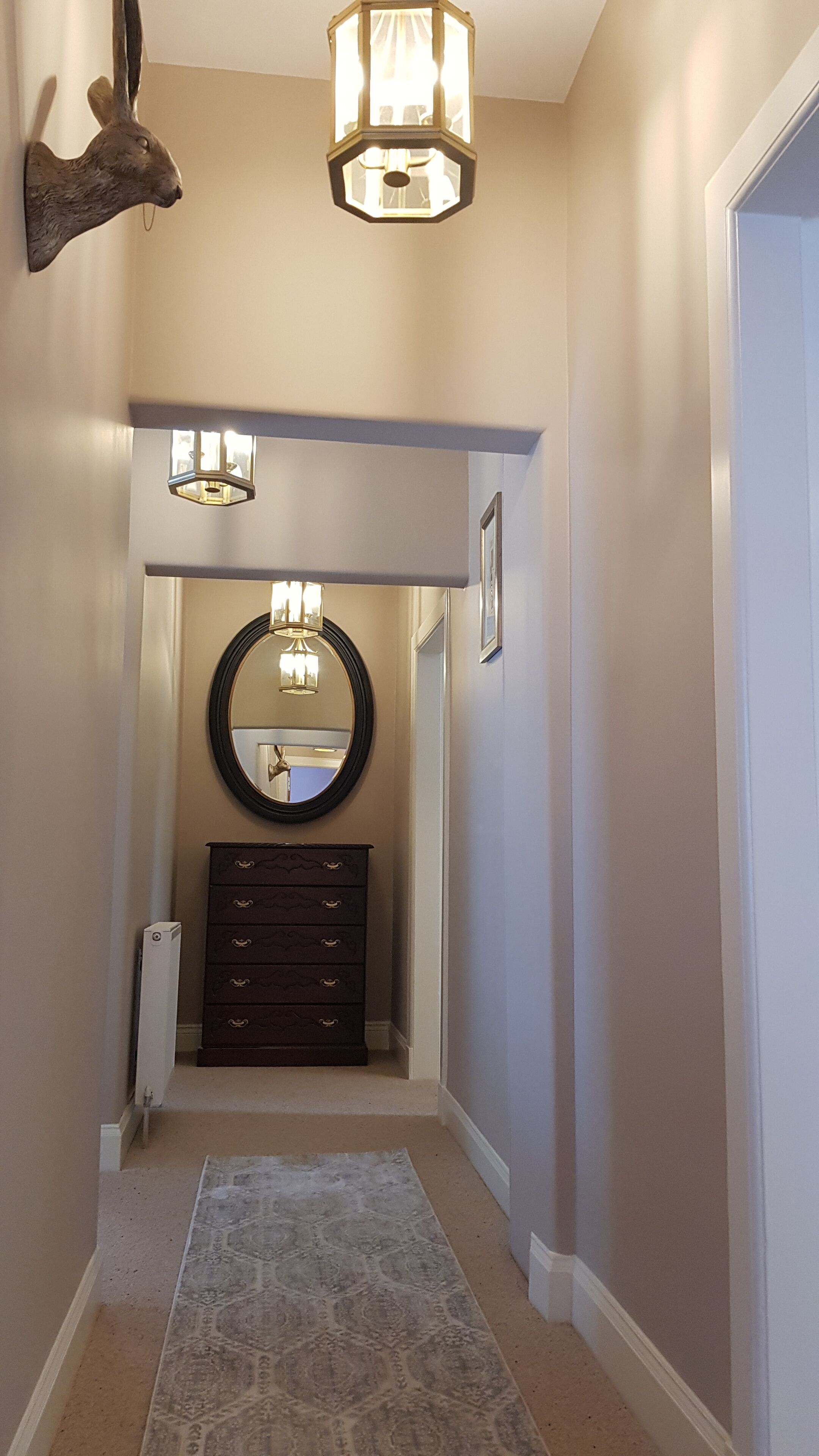A hallway with a patterned rug, a mirror, a dresser, and two wall-mounted lights.