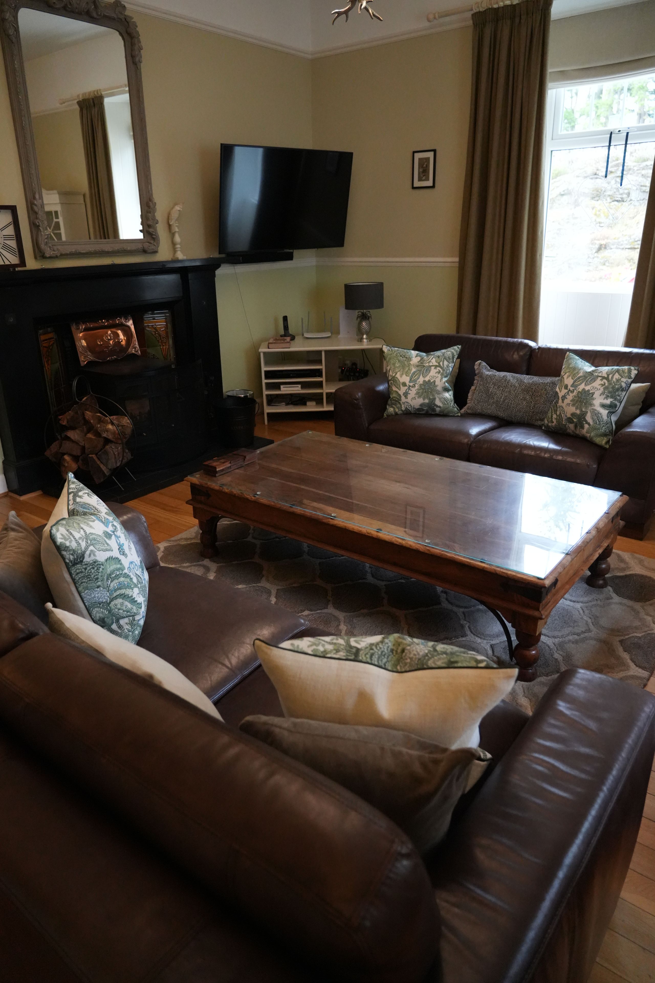 A living room with a brown leather sofa, a glass-top coffee table, and a fireplace with a mantel.