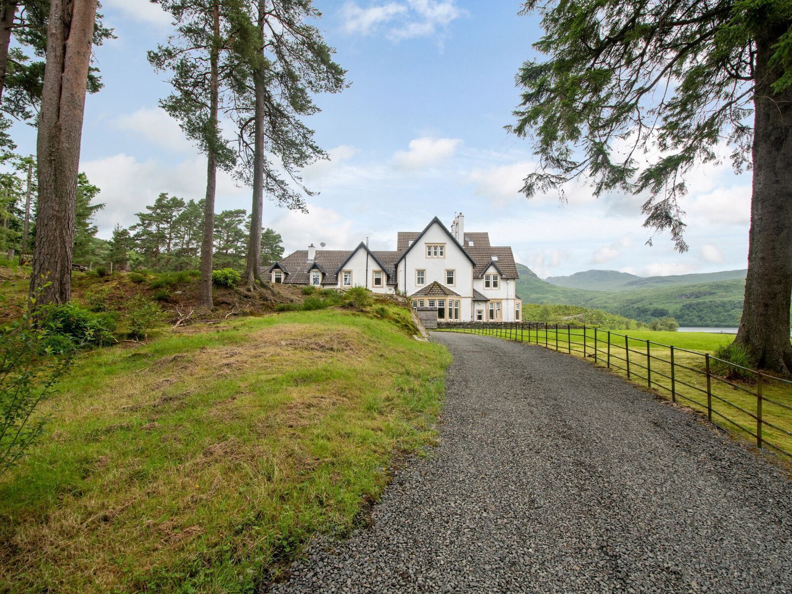 A large, white, two-story house with a gravel driveway and a metal fence.