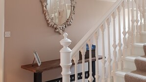 A staircase with white balusters, a wooden bench, a mirror, and a chandelier.
