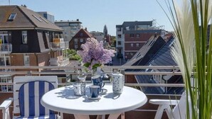 A balcony with a round table, chairs, and a vase of flowers. - Haus Belvedere - Directly behind the dune crest, only 50m to the beach crossing - (Sylt)
