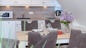 A modern kitchen with white cabinets, a microwave, and a coffee maker. There is a dining table with chairs and a vase with flowers. - Sea view, House Belvedere, directly behind the dune crest, for up to 5 people - (Sylt)