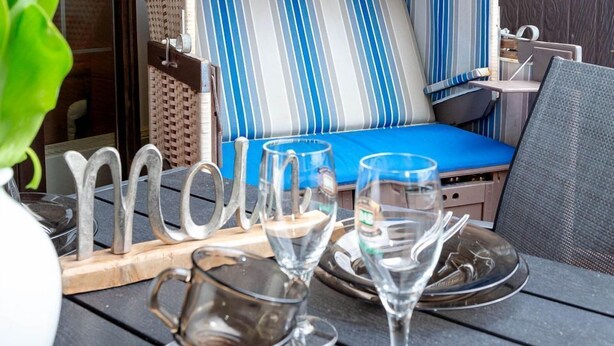 A dining table with a metal pitcher, two wine glasses, and a blue cushioned chair with striped upholstery. - Coffee, cake and the smell of the coast - Haus Belvedere (Sylt)
