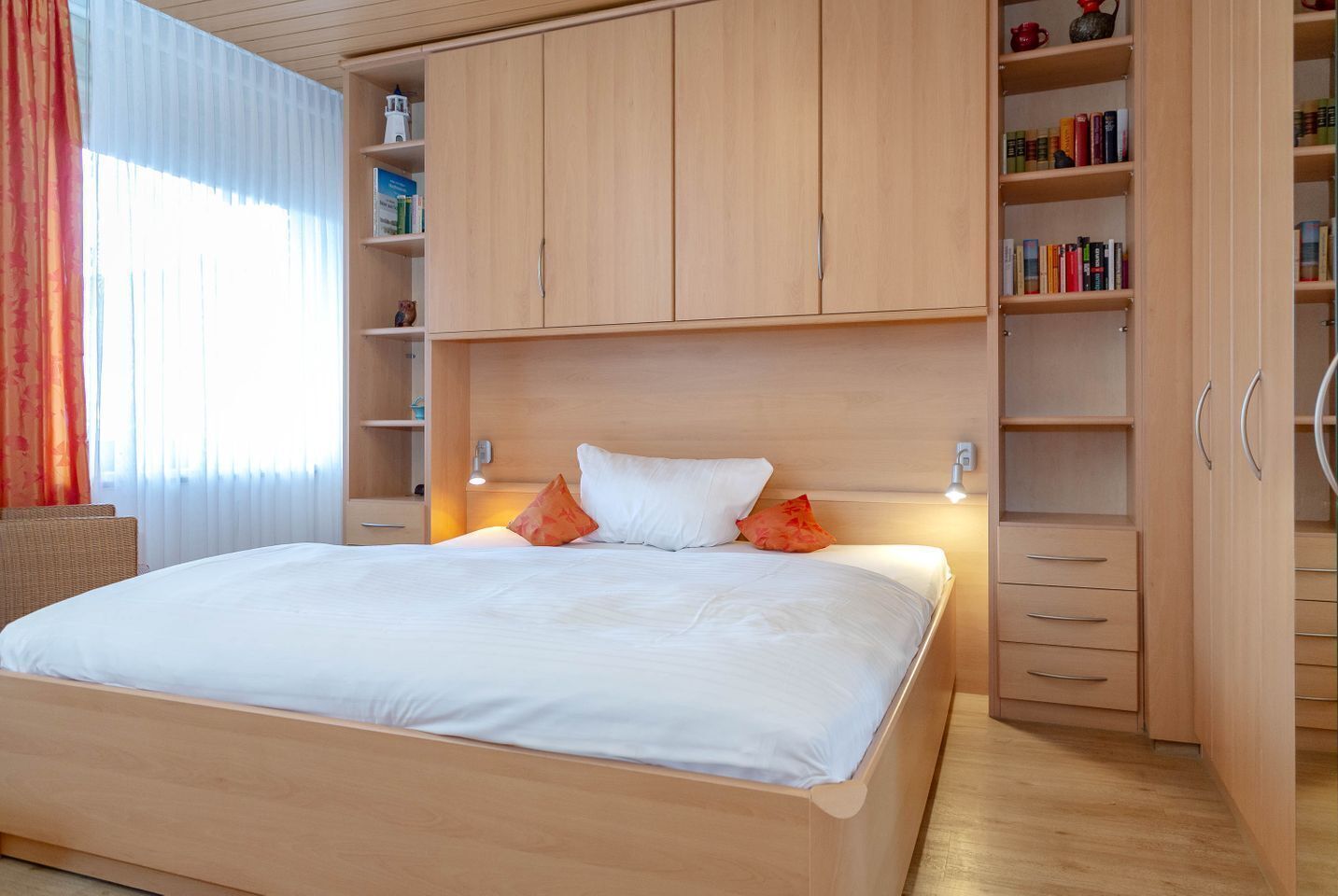Ein ordentlich eingerichtetes Schlafzimmer mit einem großen Bett, einem Holzschrank und integrierten Regalen mit Büchern und Dekorationsgegenständen.