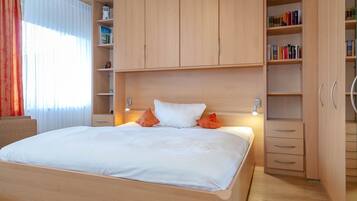 Ein ordentlich eingerichtetes Schlafzimmer mit einem großen Bett, einem Holzschrank und integrierten Regalen mit Büchern und Dekorationsgegenständen.
