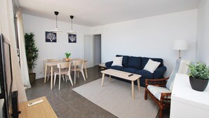 A modern living room with a blue sofa, wooden coffee table, and a dining area with a table and chairs. - Premia Palm View (Premià de Mar)
