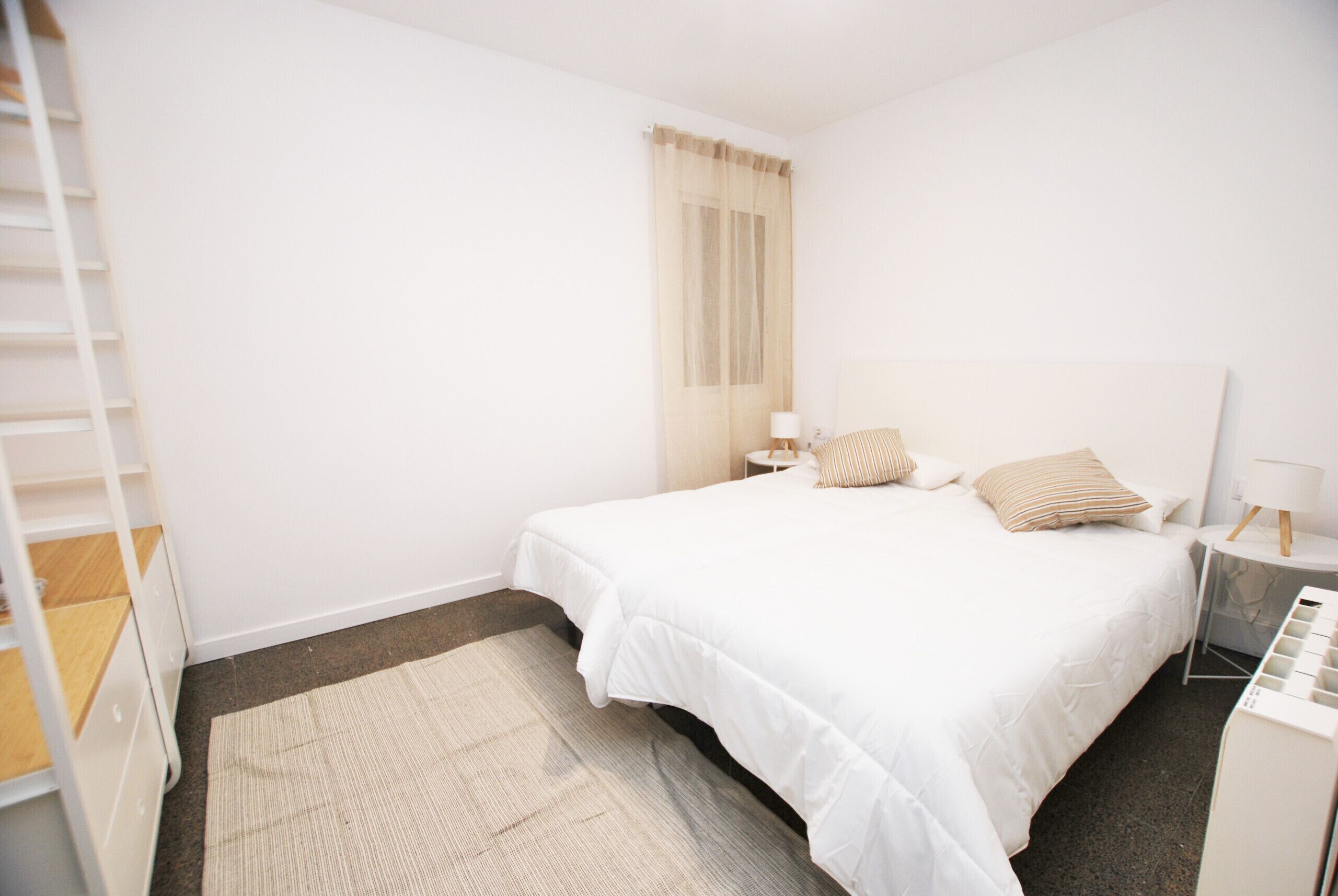 A neatly arranged bedroom with a large bed, a bedside table with a lamp, a small side table, and a wardrobe.