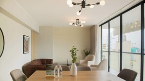 A modern dining area with a wooden table, beige chairs, a brown leather couch, and a white vase with a plant. - w* | Modern 3BR w/ Balcony Near Kennedy Park (Miraflores)