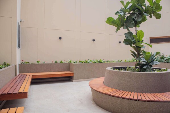 A modern outdoor seating area with wooden benches and a circular planter with a tree.