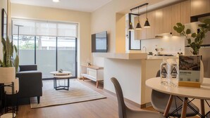 A modern living room with a sofa, coffee table, and a dining area with chairs and a table. There is a large window with a view of the outside.