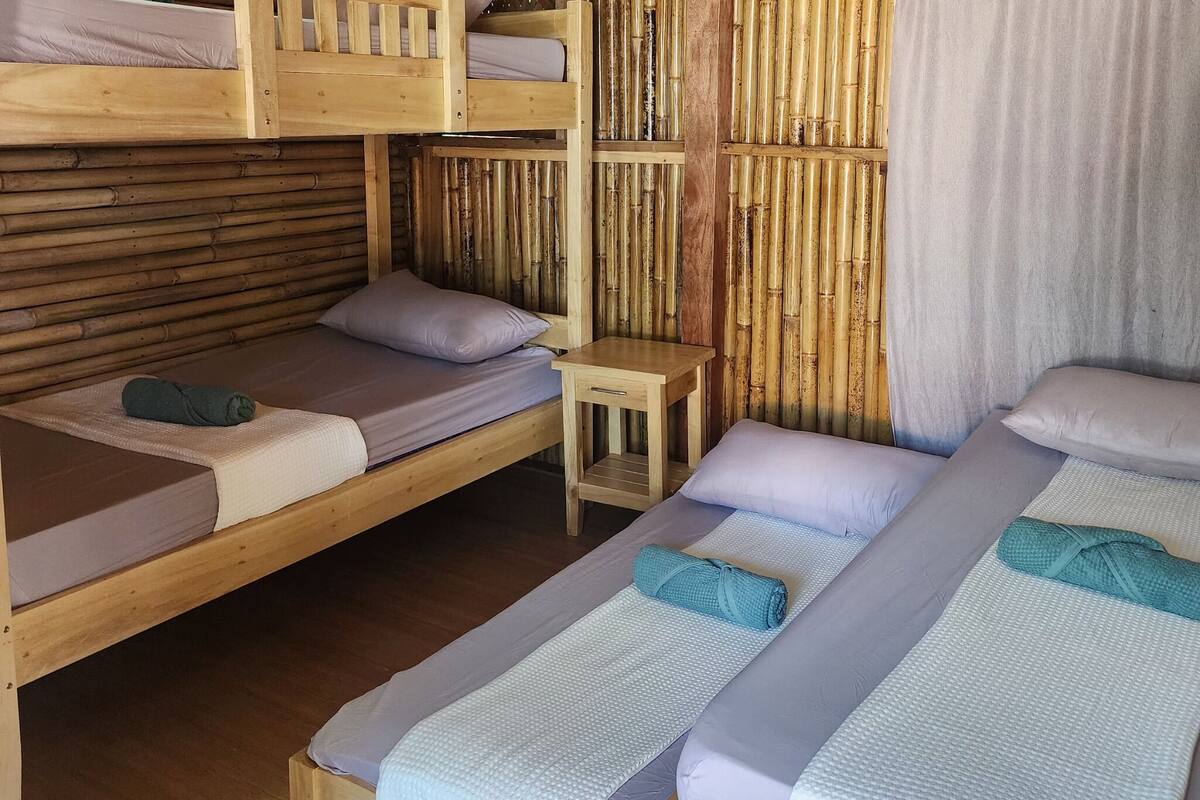 Quarto com duas camas de solteiro, uma cama beliche e uma mesa pequena.
