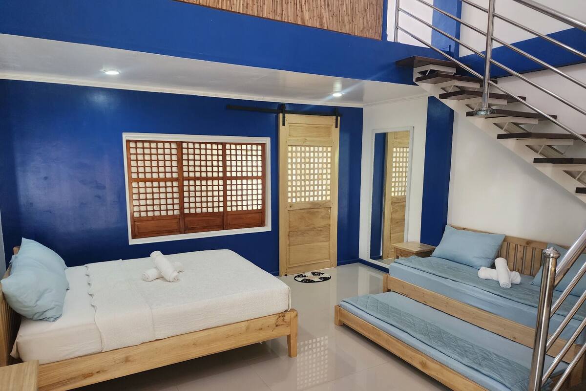Quarto com duas camas de madeira, decoração azul e branca, uma porta de madeira e uma escada.
