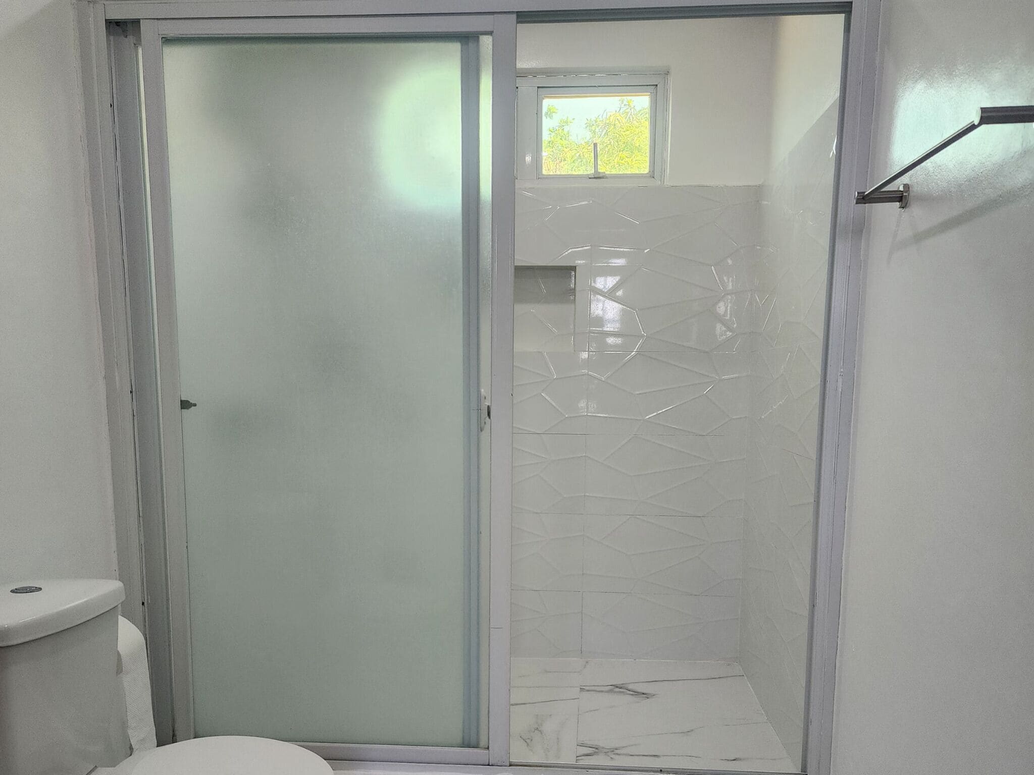 A bathroom with a glass shower enclosure, a toilet, and a small window.