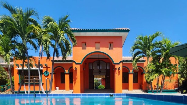 A hotel with a pool, palm trees, and a bright orange facade. - Kulibangbang Beach Resort (Bacnotan)