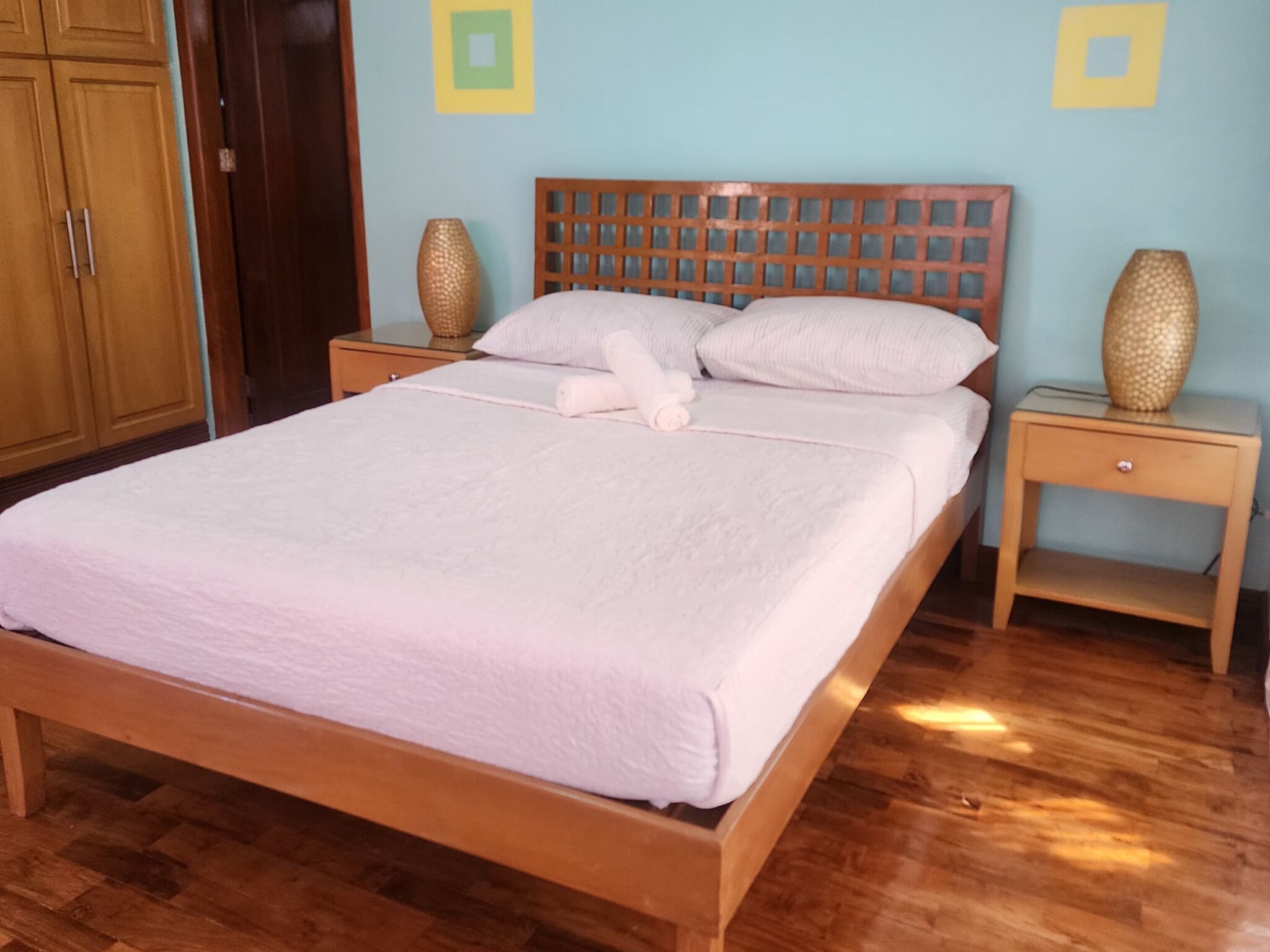 A neatly made bed with a wooden headboard, two bedside tables with decorative vases, and a wooden wardrobe.
