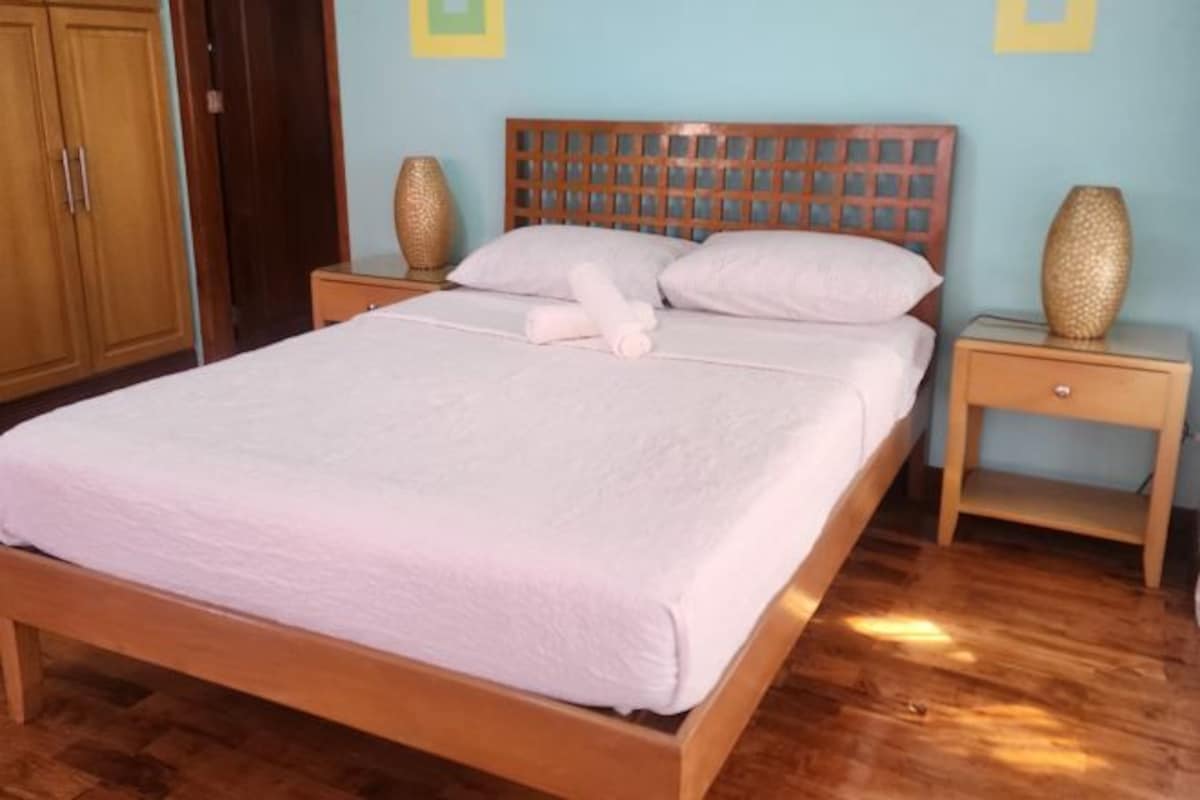 A neatly made bed with a wooden headboard, two bedside tables with decorative vases, and a wooden wardrobe.