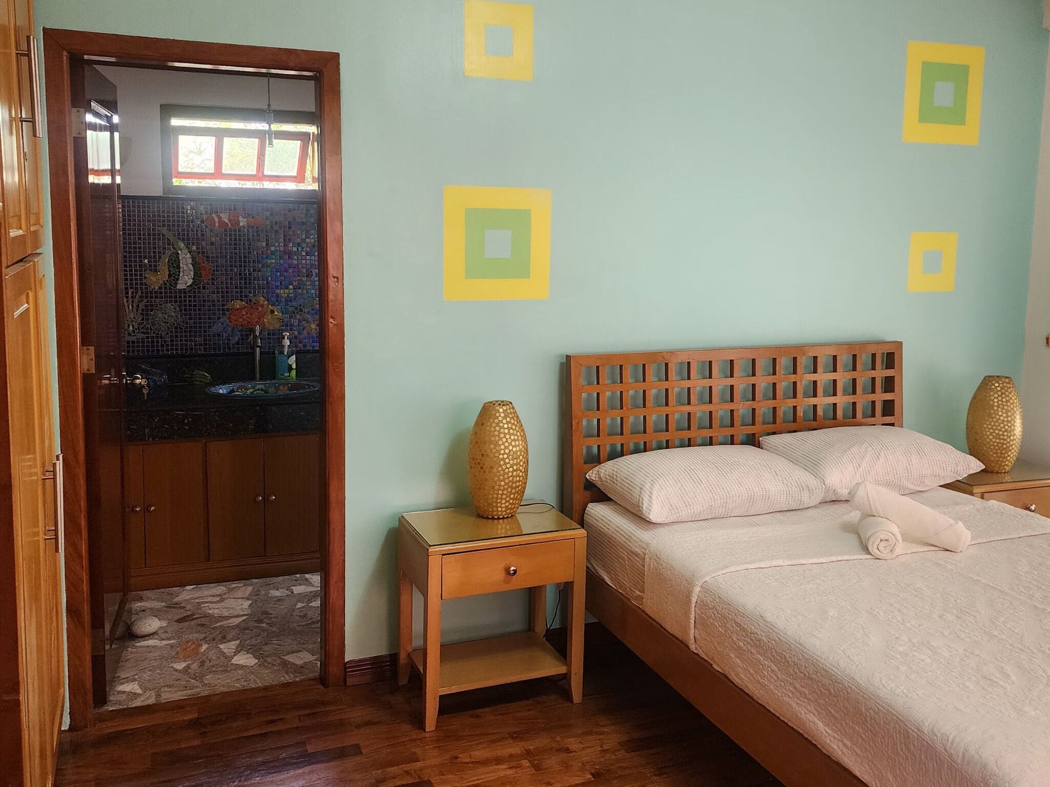 Quarto com cama de madeira, mesa de cabeceira, um vaso decorativo e área do chuveiro com azulejos.