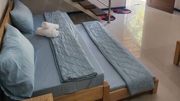 Ein Zimmer mit zwei hölzernen Betten, jeweils mit blauer Matratze und Kissen. In der Ecke steht eine Holzbank und im Hintergrund ist ein Metallgeländer zu sehen.
