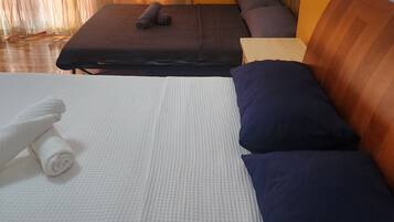Ein ordentlich bezogenes Bett mit weißen und dunkelblauen Kissen, ein aufgerolltes weißes Handtuch und ein gefaltetes dunkelblaues Handtuch.