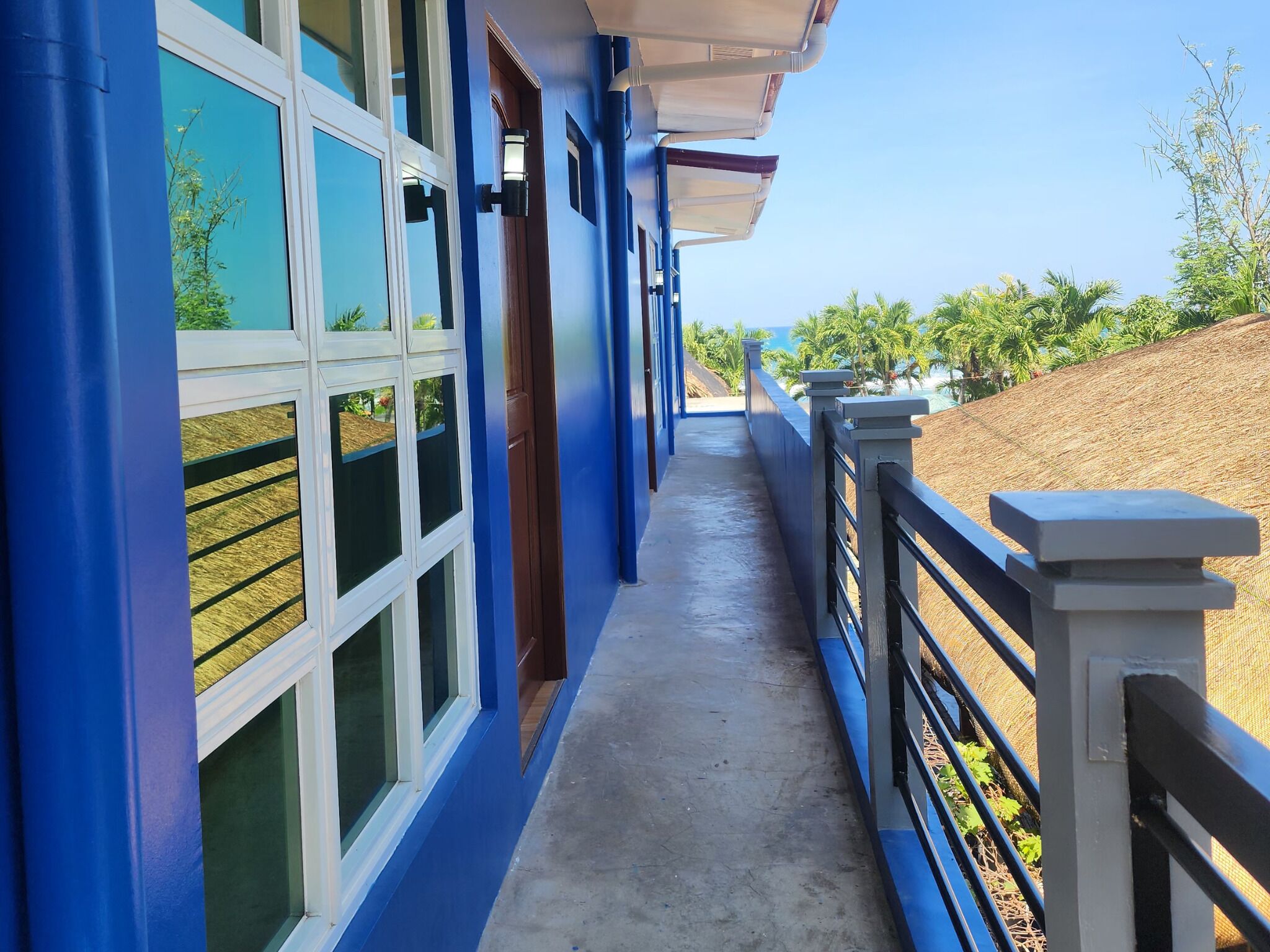 A building with blue exterior walls, a covered walkway, and a view of a landscaped area with palm trees.