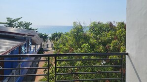 A balcony with a view of the sea, a building with a blue facade, and lush greenery. - Kulibangbang Beach Resort (Bacnotan)