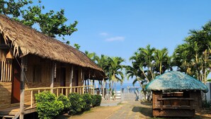 A wooden building with a thatched roof, surrounded by palm trees and a clear sky. - Kulibangbang Beach Resort (Bacnotan)