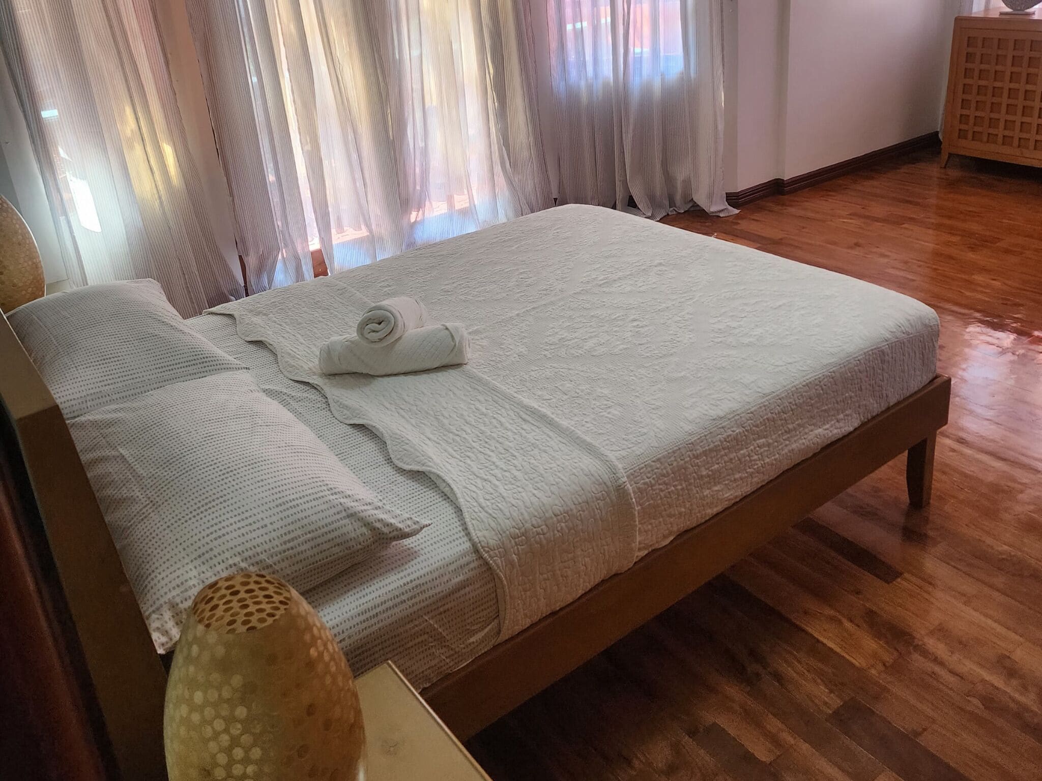Ein ordentlich bezogenes Bett mit gerolltem Handtuch, Holz-Kopfbrett und Holzboden.