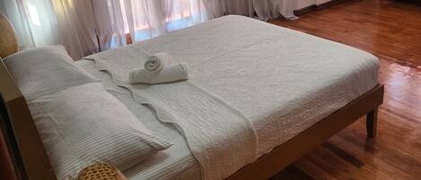 Ein ordentlich bezogenes Bett mit gerolltem Handtuch, Holz-Kopfbrett und Holzboden.