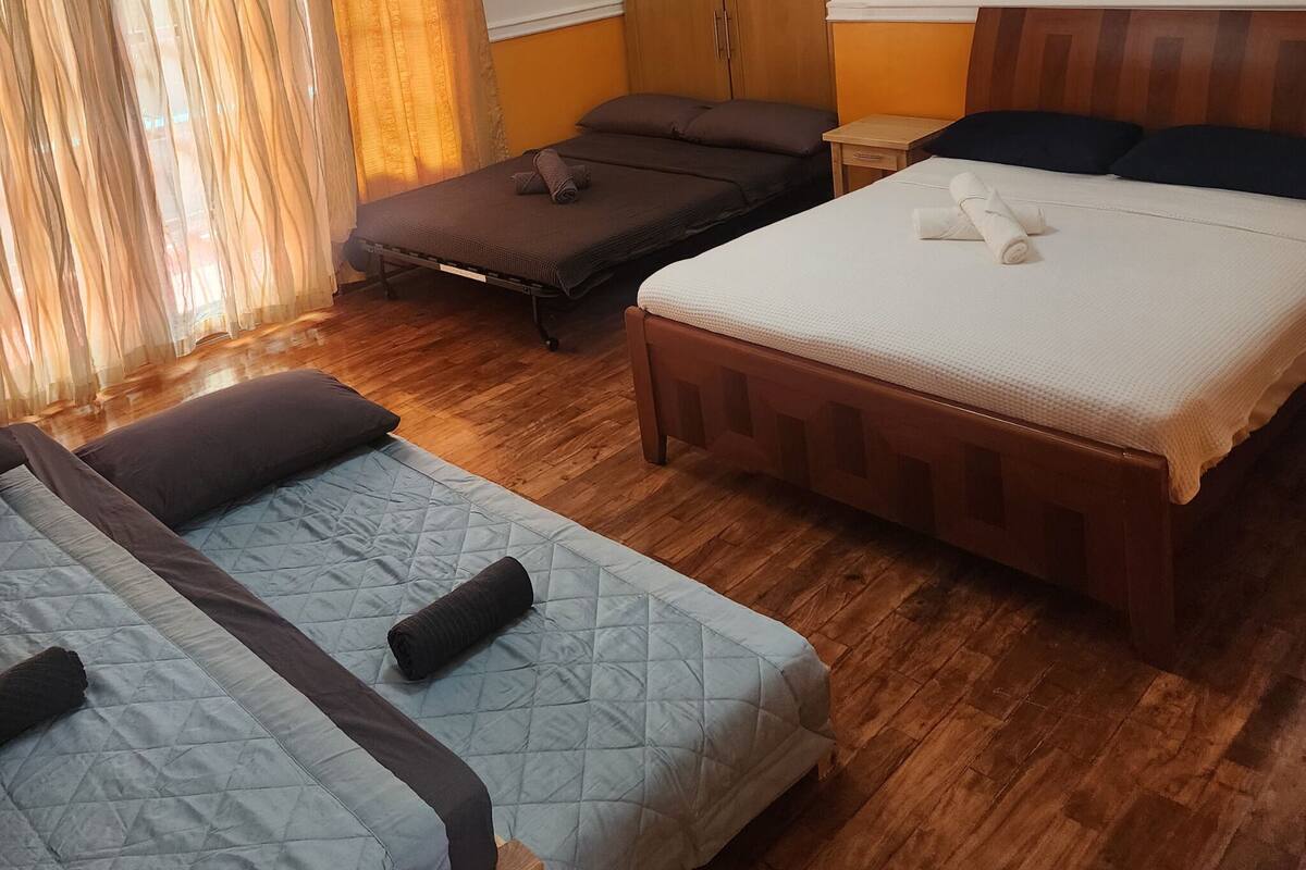 Quarto de hotel com duas camas, um sofá-cama, piso de madeira e cabeceira de madeira.