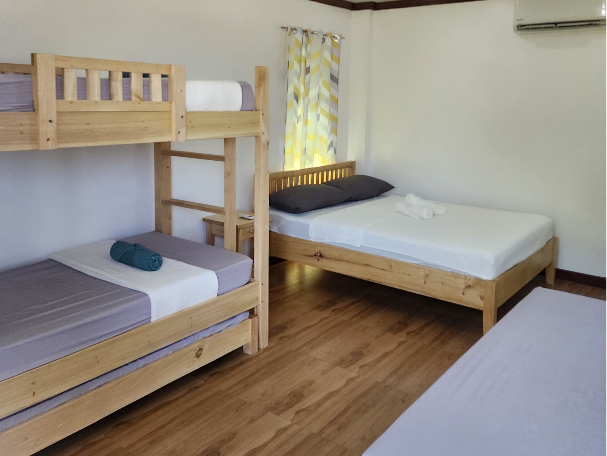 Une chambre avec deux lits superposés et un lit simple, un plancher en bois et une fenêtre avec des rideaux.