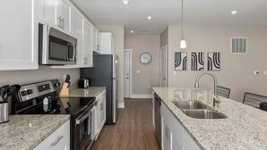A modern kitchen with white cabinets, stainless steel appliances, granite countertops, and a double sink. - Modern 16BR 16BA Condos w Garage and Patio (Wyoming)