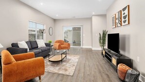 A modern living room with a sofa, armchairs, a coffee table, a TV, and artwork on the wall. - Modern 16BR 16BA Condos w Garage and Patio (Wyoming)