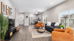A modern living room with a sofa, armchair, and a coffee table. There is a kitchen in the background with white cabinets and a dining area with chairs. - Modern 16BR 16BA Condos w Garage and Patio (Wyoming)
