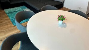 A modern living room with a sectional sofa, a round table with chairs, a small potted plant, and a beach-themed painting on the wall. - LivingMe Cozy 3 rooms to relax in (Korntal-Münchingen)