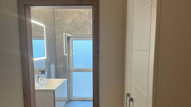 A hallway leading to a bathroom with a window, a sink, and a door with a handle. - LivingMe Cozy 3 rooms to relax in (Korntal-Münchingen)