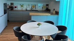 A modern kitchen with a central island, a dining area with a round table and six chairs, and a kitchen counter with various appliances. - LivingMe Cozy 3 rooms to relax in (Korntal-Münchingen)