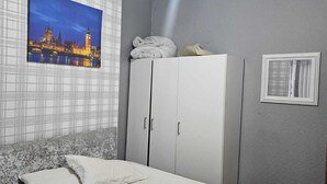 A bedroom with a bed, a wardrobe, a painting of a cityscape, and a window with curtains.
